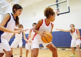 Female High School Basketball Team Playing Game In Gymnasium